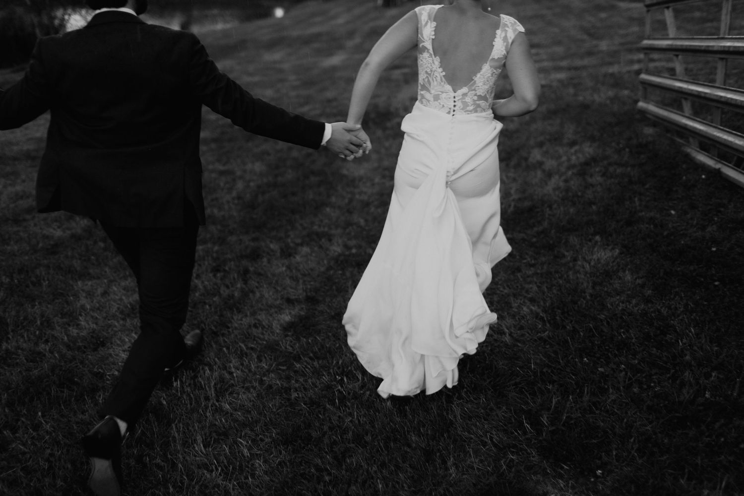 Black and white wedding photo showing couple walking hand in hand across grass with flowing white bridal gown.