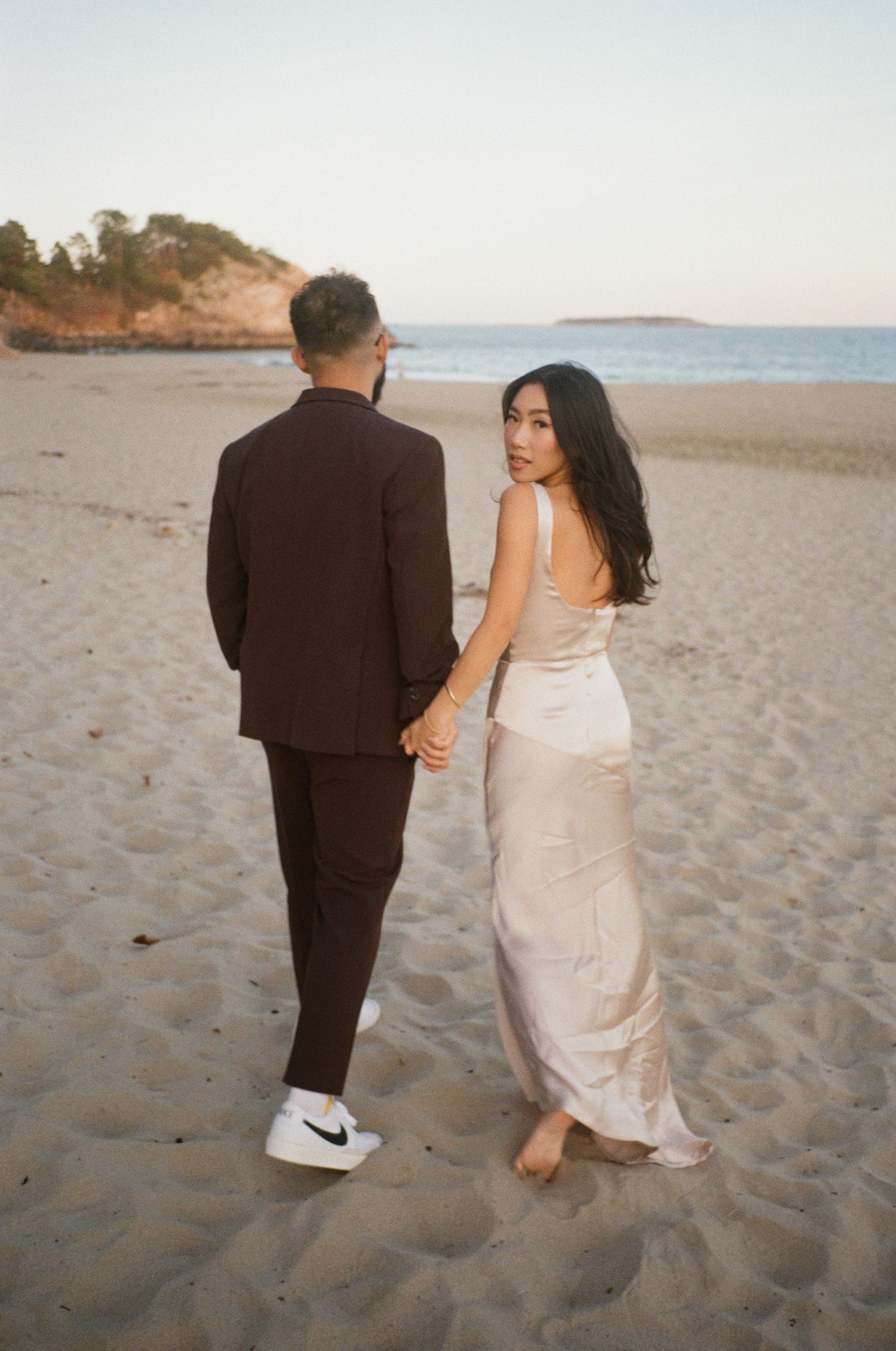 Couple strolling along peaceful beach at dusk wearing formal attire in Beverly, MA.