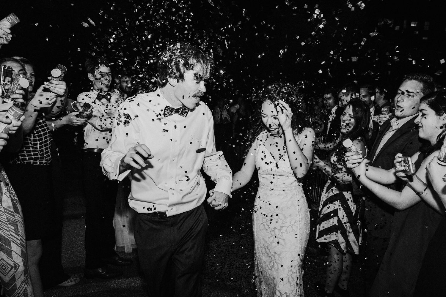Wedding reception guests dance and celebrate as they exit their wedding celebration under confetti at night.