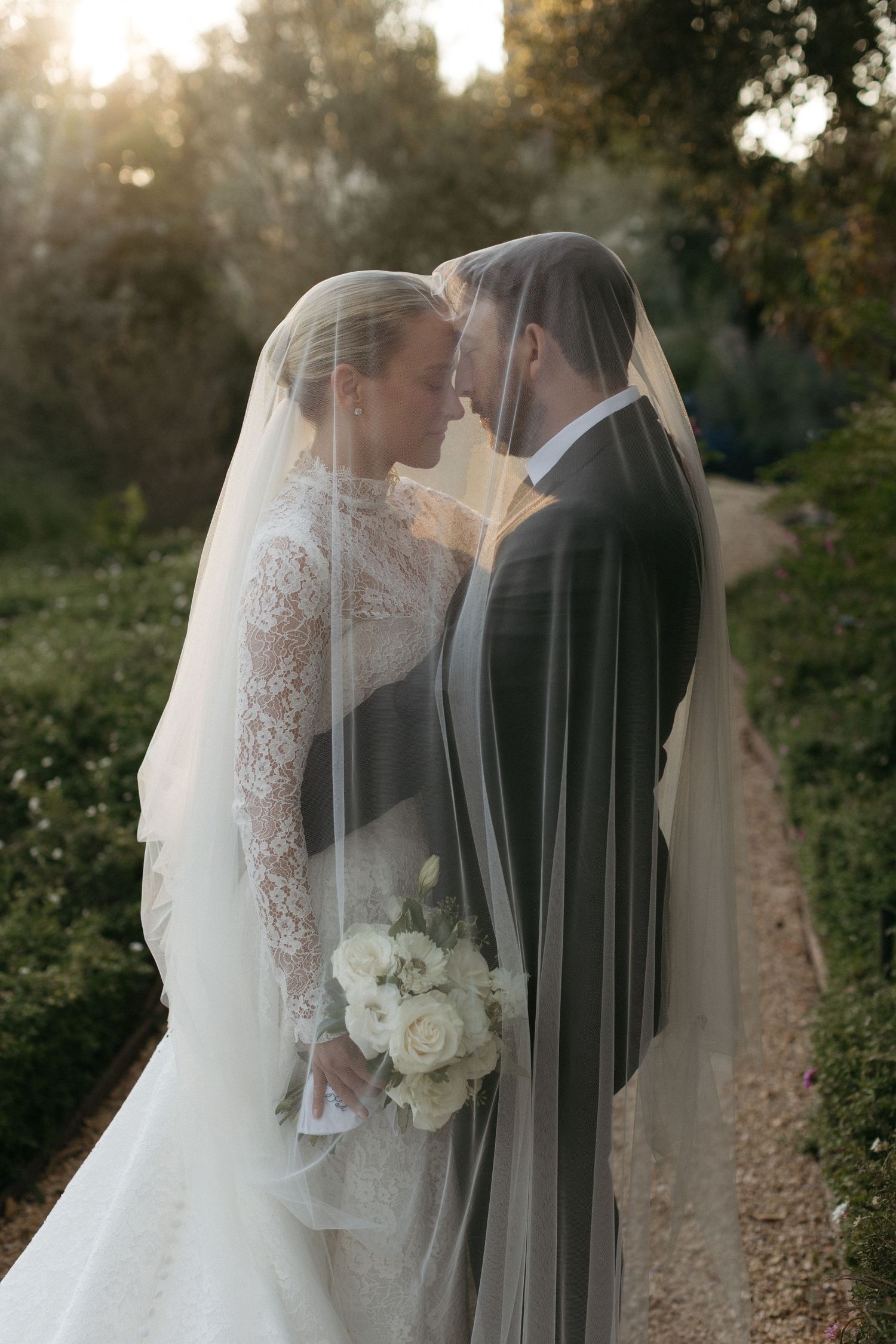 A romantic wedding portrait through a sheer veil with white roses in golden sunlight in Santa Barbara, CA.