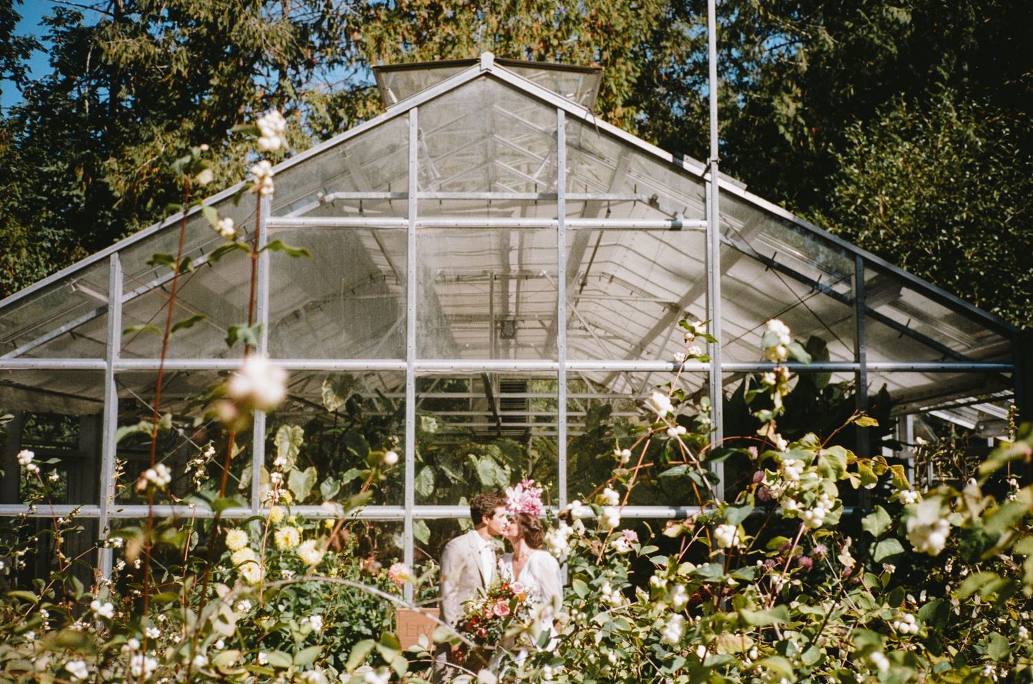Large greenhouse structure surrounded by lush garden and flowering plants.
