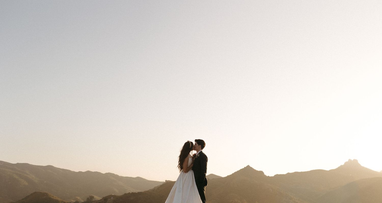 A silhouetted couple embraces against a mountainous desert landscape at sunset.