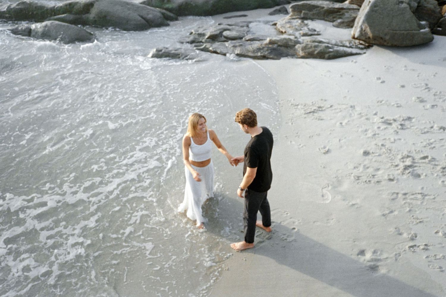 Couple walking along a rocky beach coastline in San Diego, CA during their engagement session.