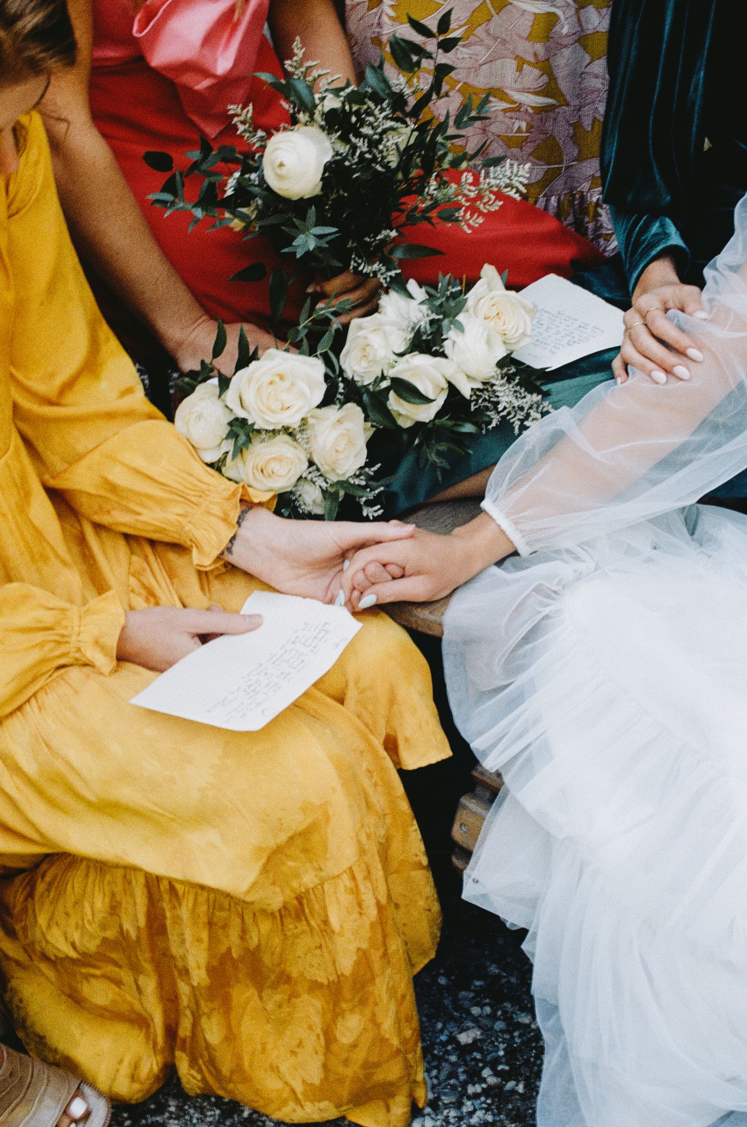 Two people sit together holding papers in white and yellow dresses near a waterfront.