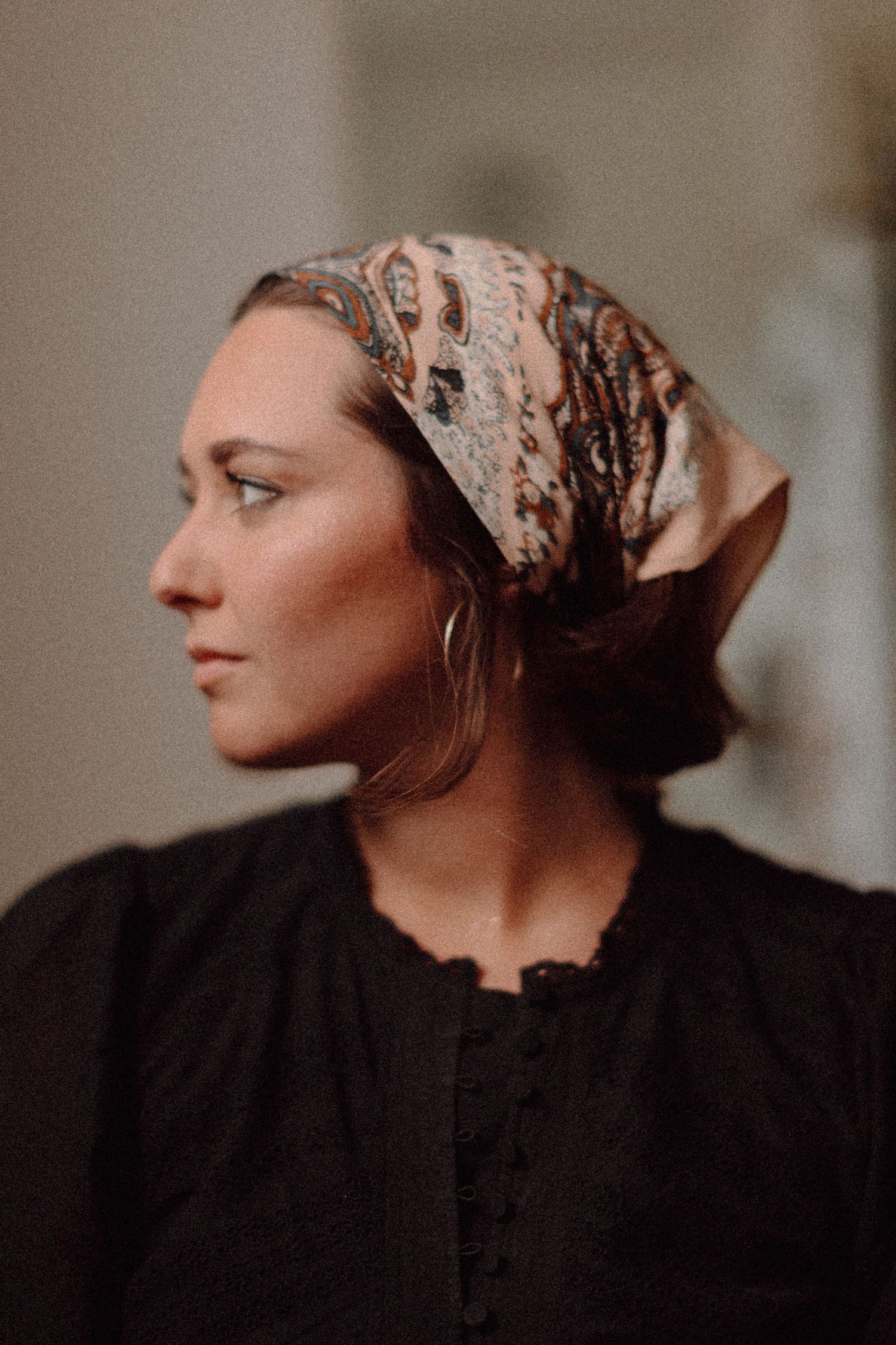 Profile view of someone wearing a black top and patterned headscarf looking to the side in Los Angeles, CA.