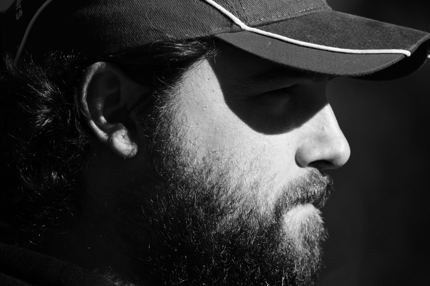Black and white profile portrait of a bearded man wearing a cap, captured in dramatic side lighting.