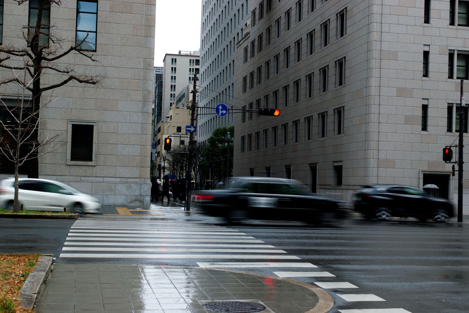 Wet city street intersection with motion-blurred cars on a rainy day.