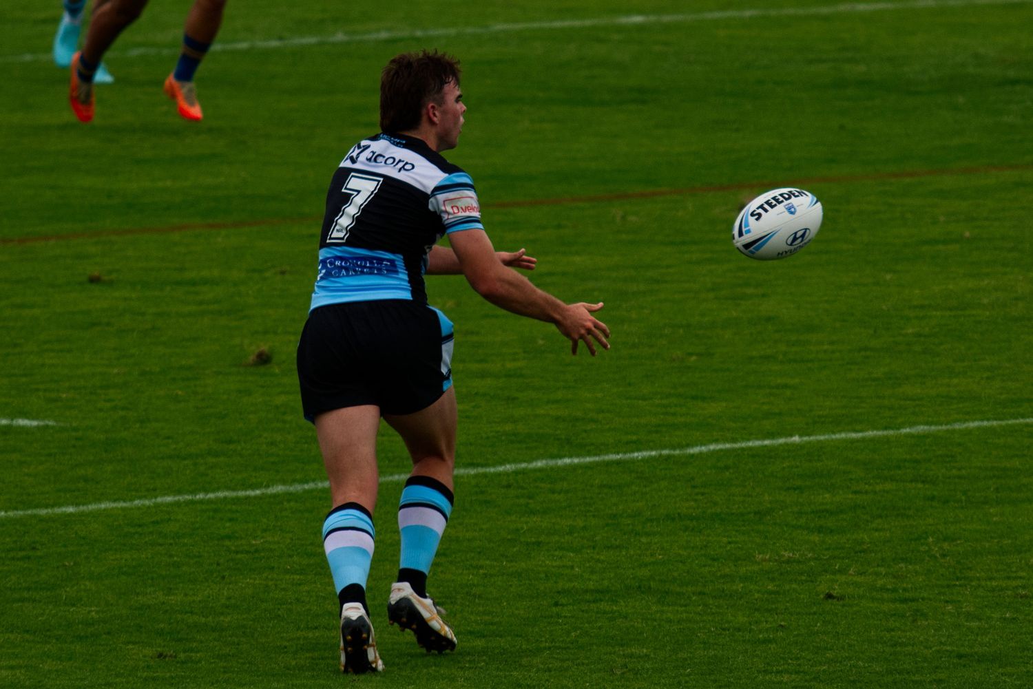 A rugby league player in teal jersey passes the ball during a competitive match.