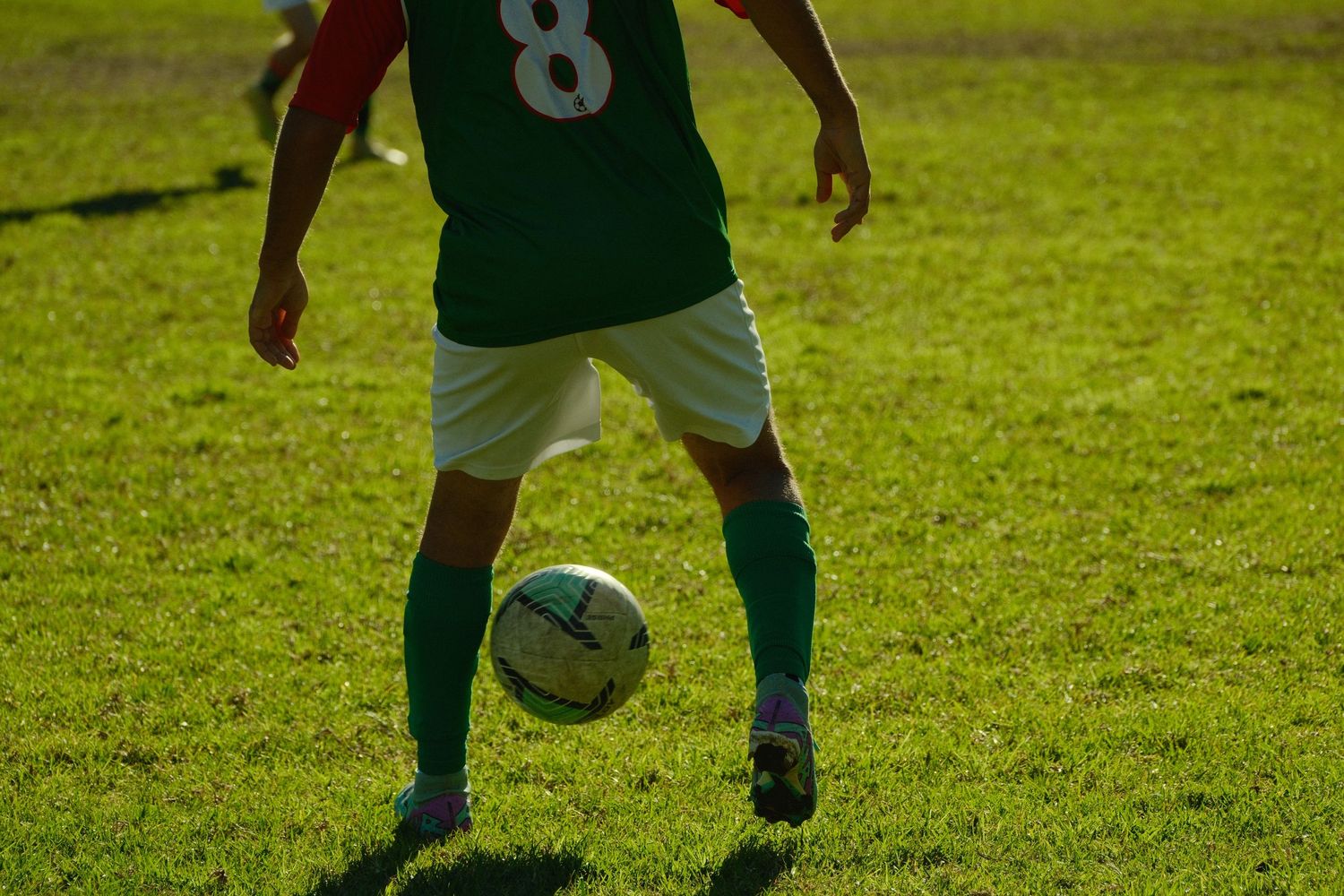 Soccer player wearing number 8 green jersey dribbling a ball on a lush green grass field.