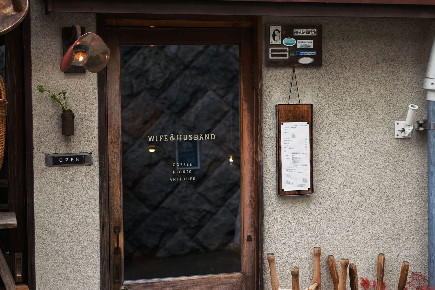 Cozy cafe entrance with dark stone wall, wooden door, and Wife & Husband signage in a charming storefront.