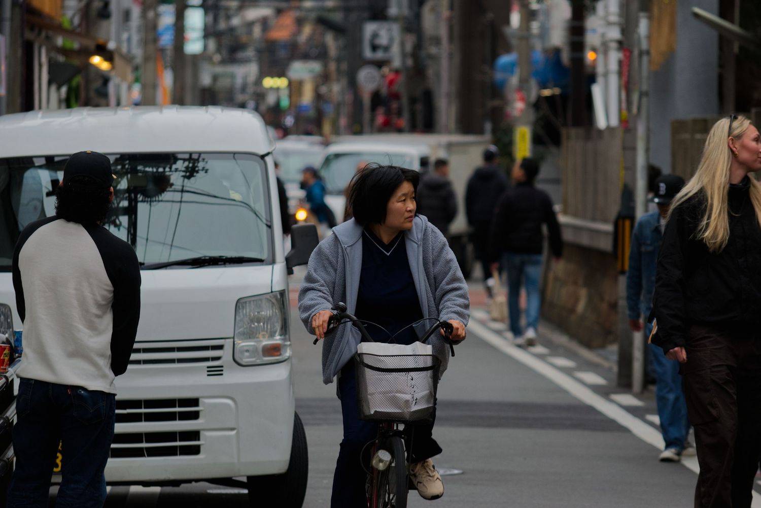 Woman riding a bicycle through a busy urban Japanese street near a white van.