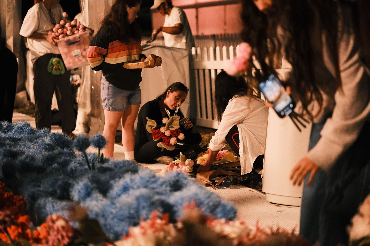 People arranging colorful flowers at an outdoor night market or flower event.