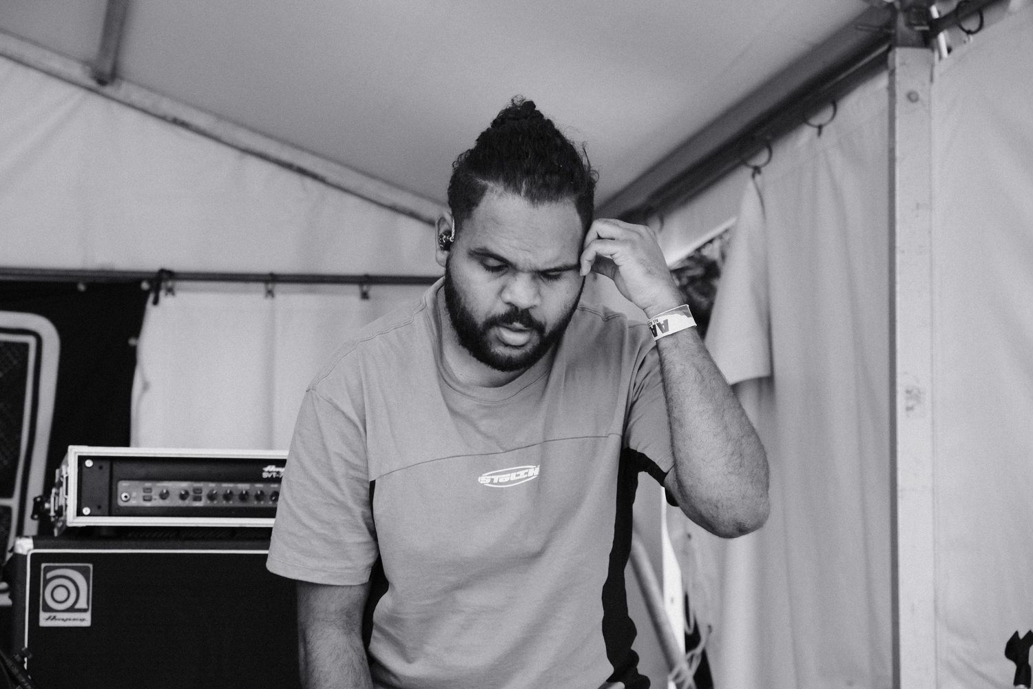 Man in casual t-shirt standing backstage near amplifiers in black and white photo.