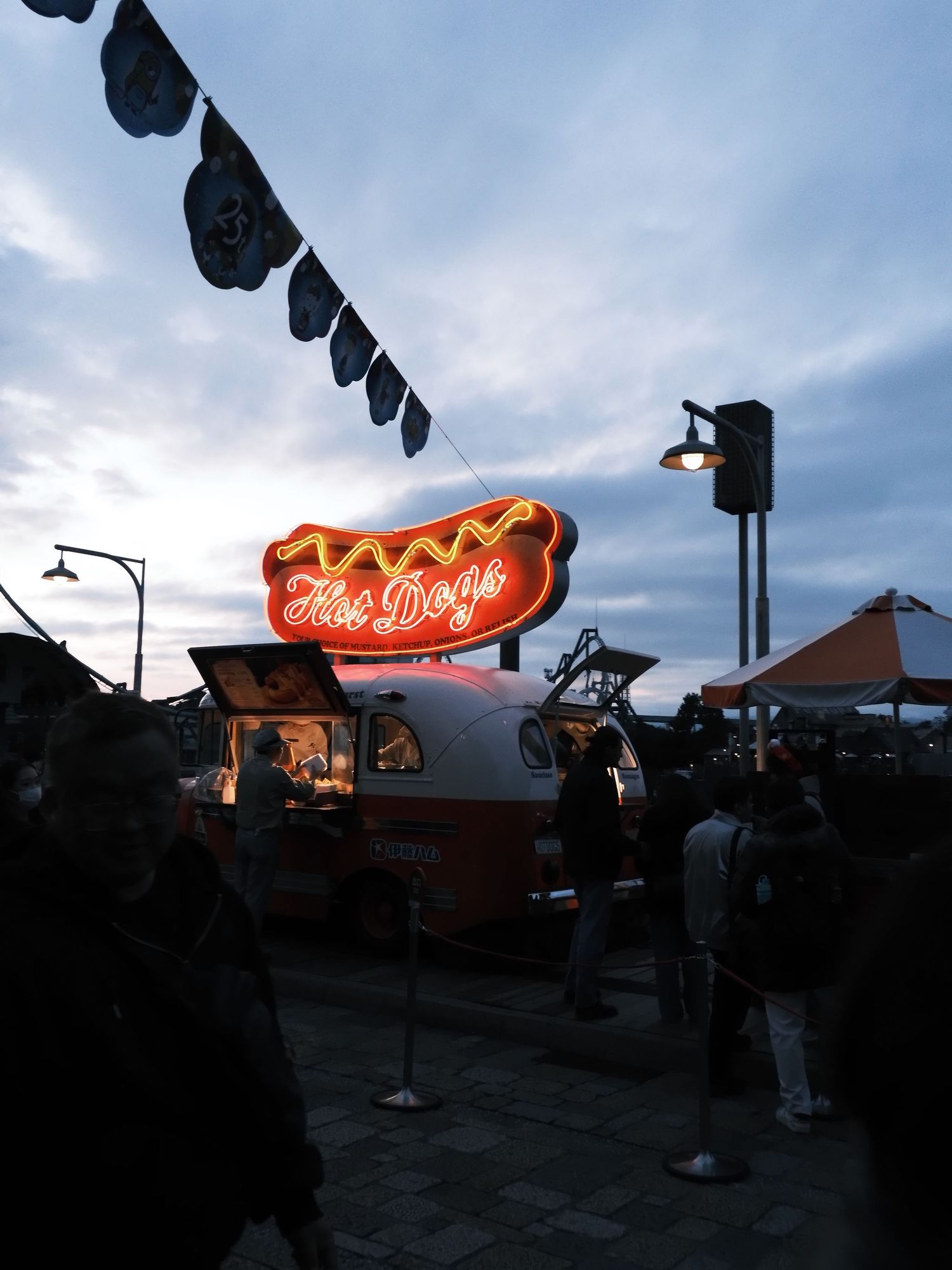 Glowing neon hot dogs sign above a food truck at an outdoor evening market event.