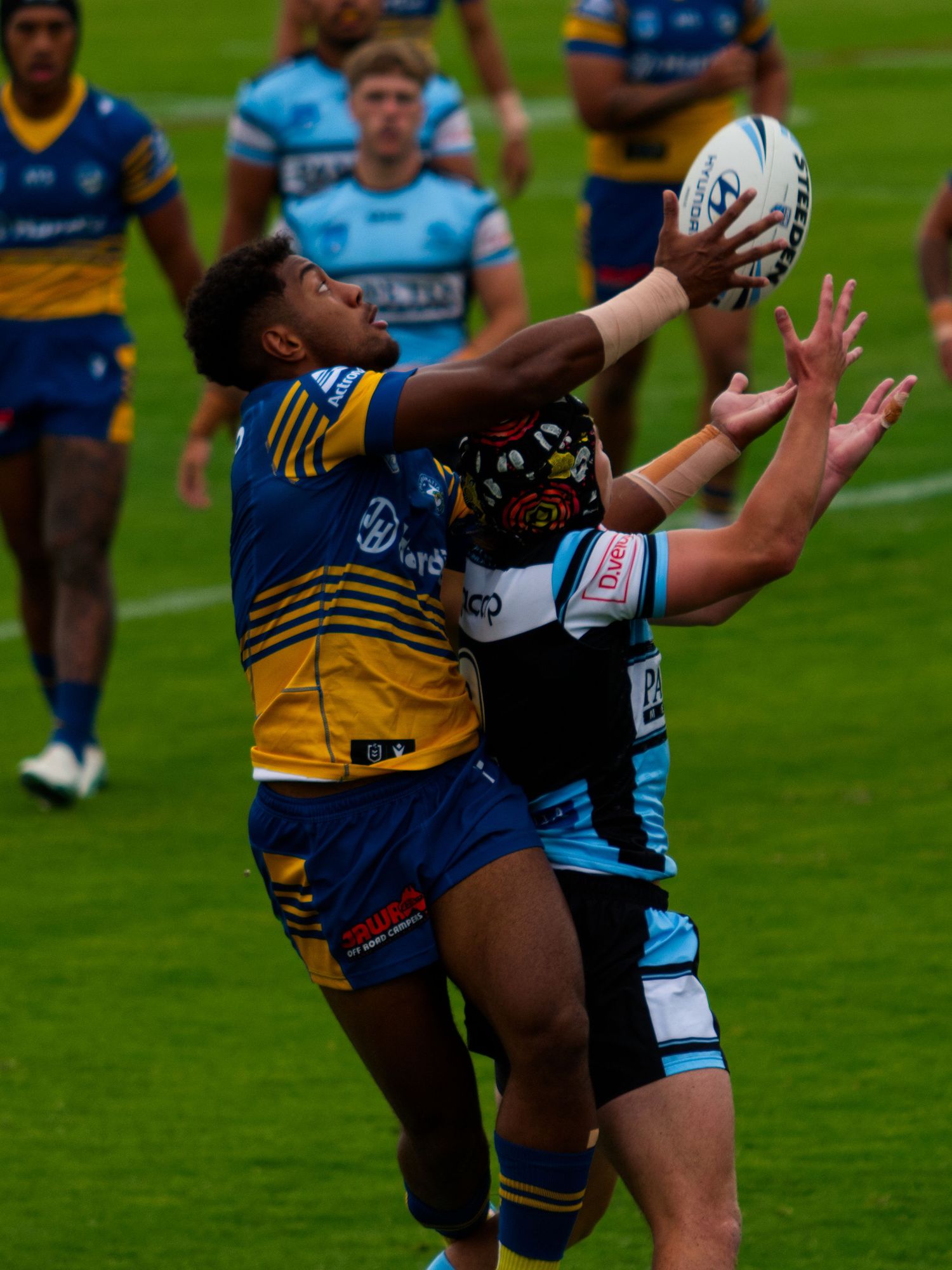 Two rugby league players contest a high ball during an intense match on green turf.