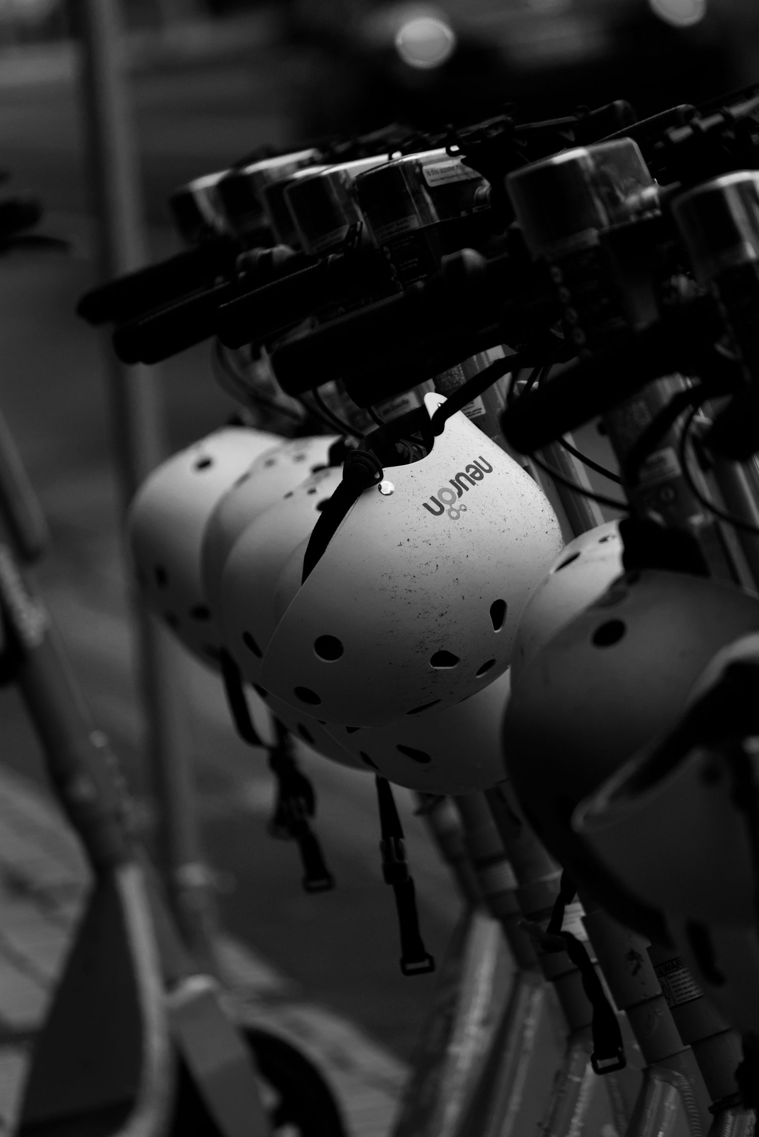 Black and white photo of rental scooter helmets lined up on handlebars.
