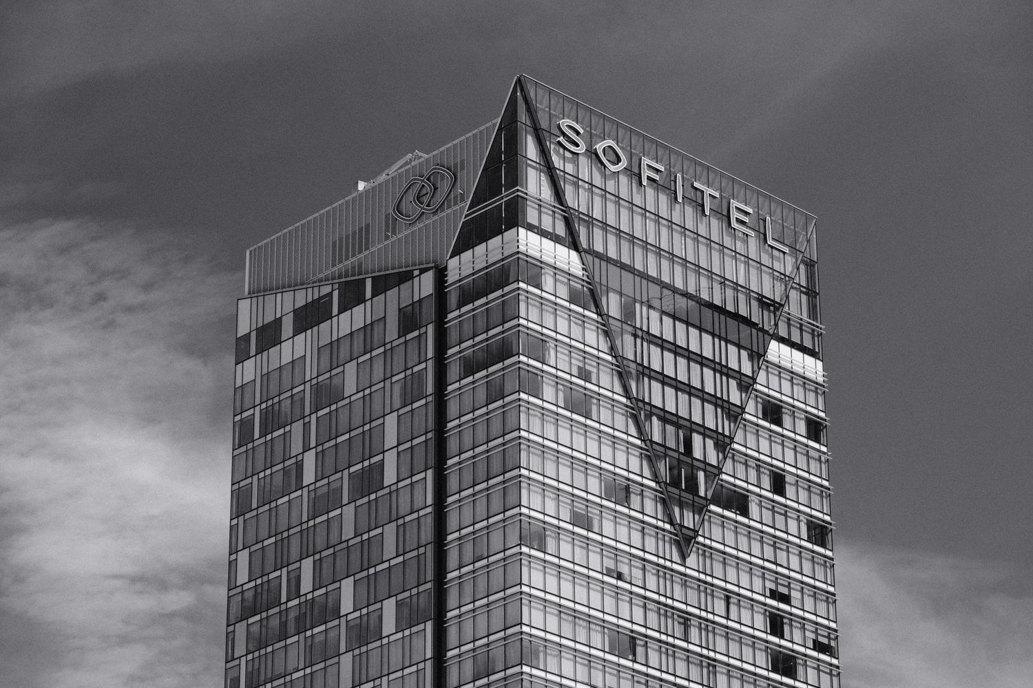 Black and white photo of the Sofitel hotel skyscraper with glass facade and triangular design against cloudy sky.
