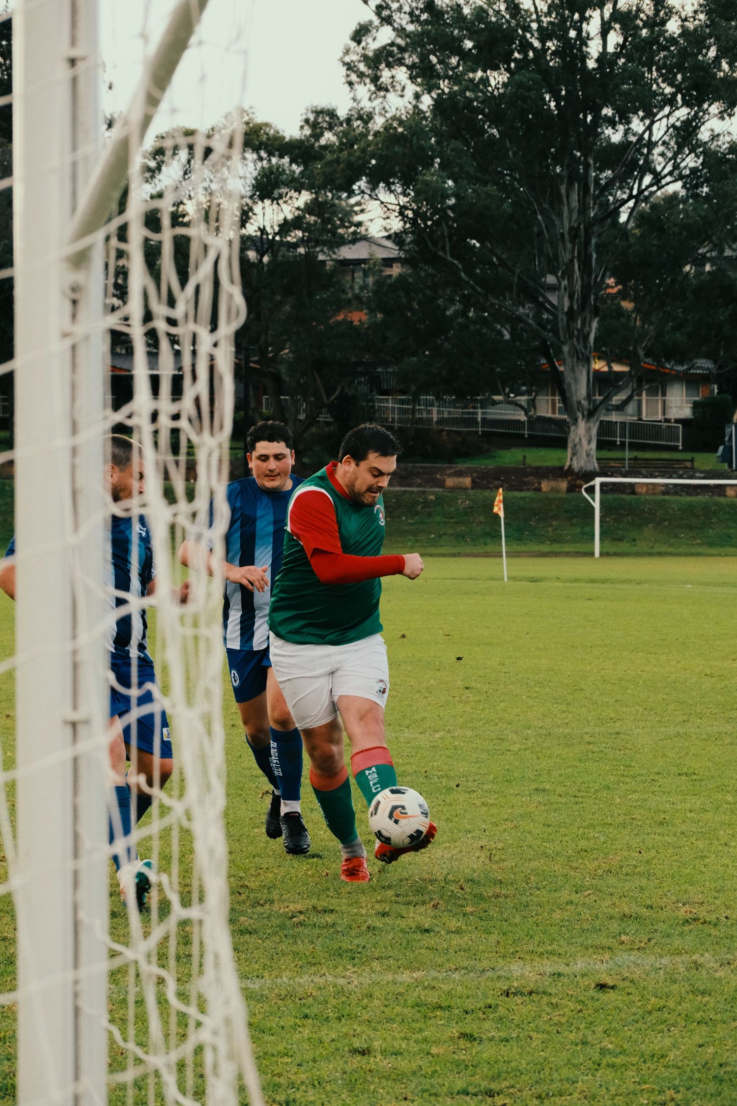 Soccer player in green jersey dribbling ball toward goal net during outdoor match on grass field.