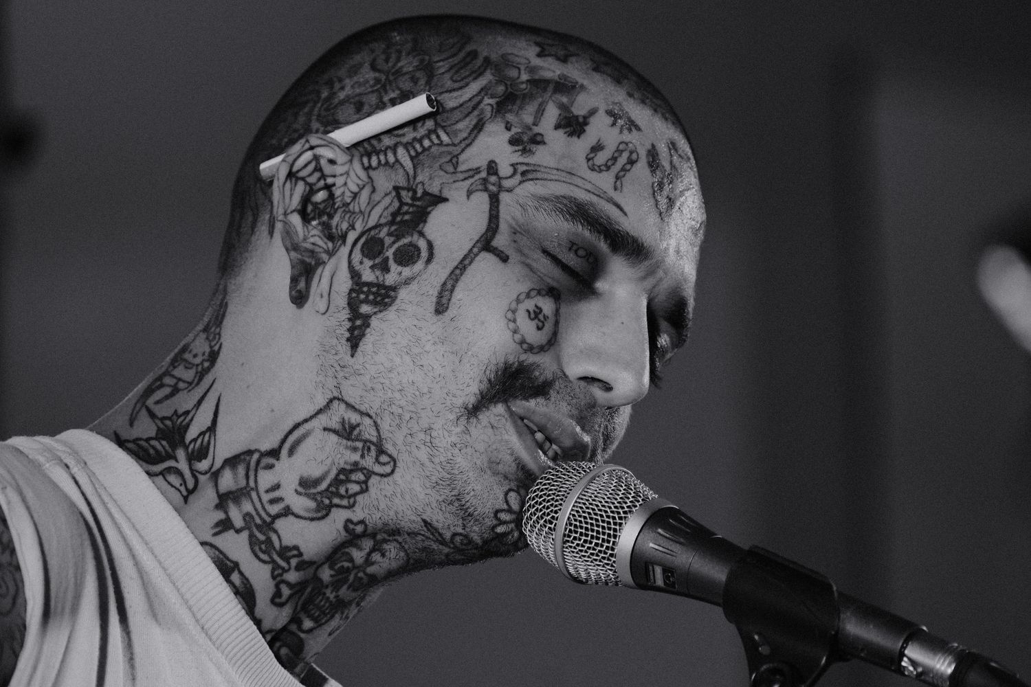Black and white photo of a heavily tattooed man singing into a microphone at a live music performance.