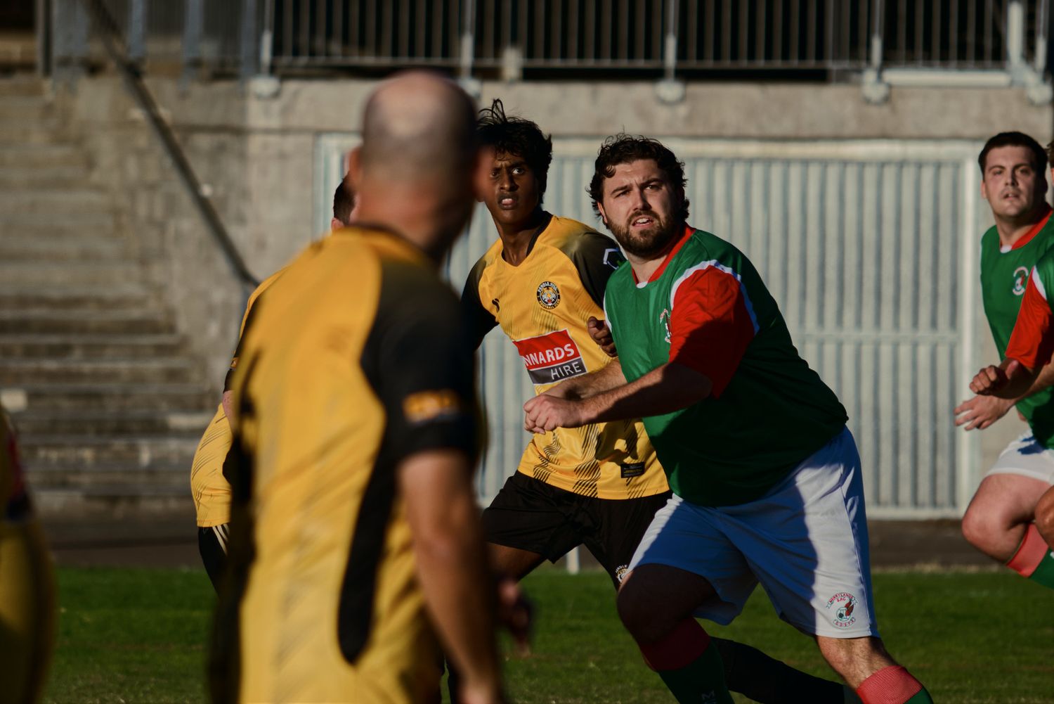 Soccer players in green and yellow uniforms compete in a physical challenge during an outdoor match.