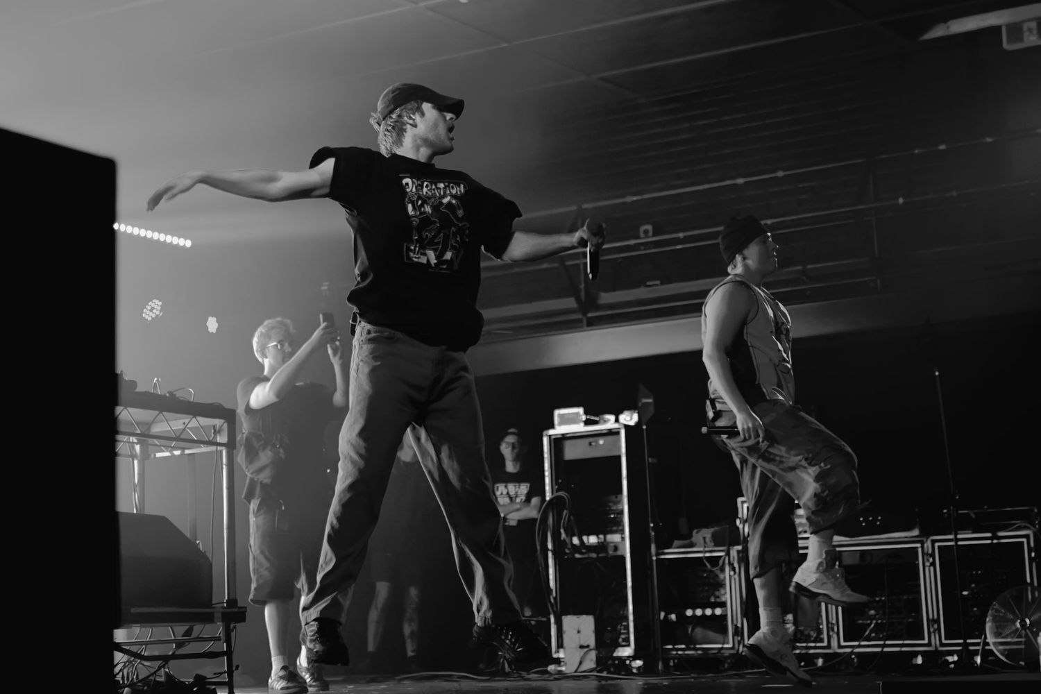 Black and white photo of performers dancing energetically on a concert stage with dramatic lighting.