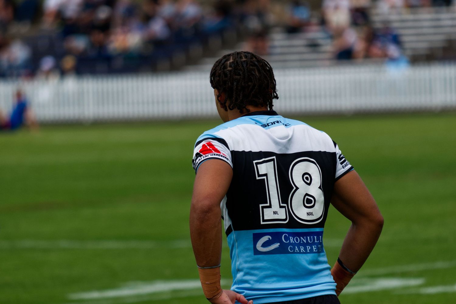 A rugby league player wearing number 18 in a teal Cronulla Sharks jersey stands on field.