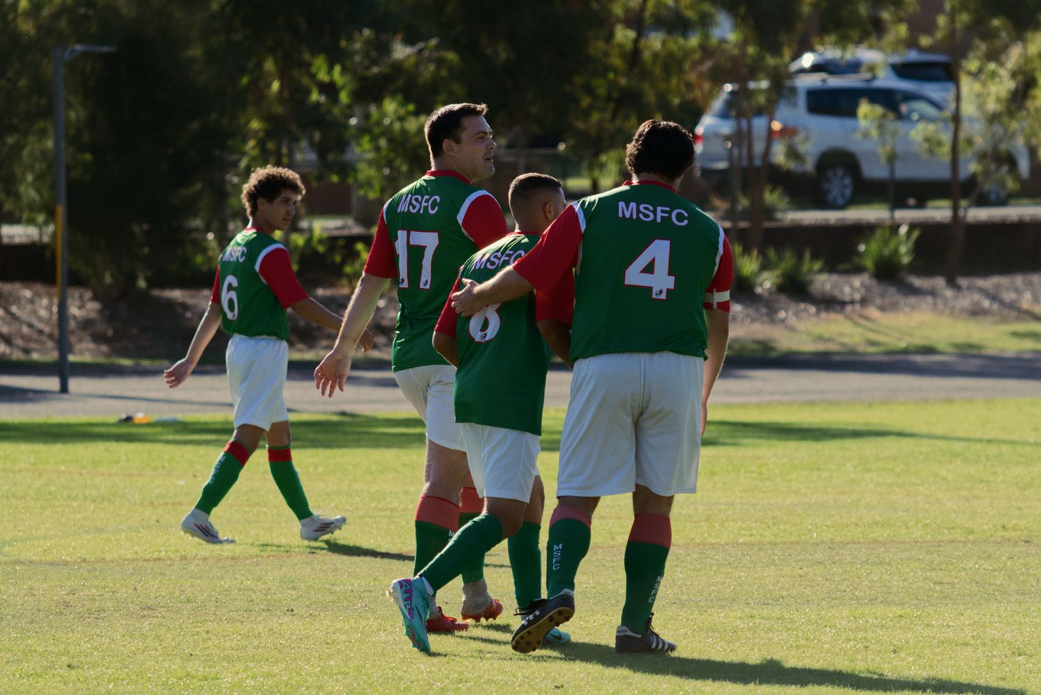 MSFC soccer players in green and red jerseys celebrate together on the field after a goal.