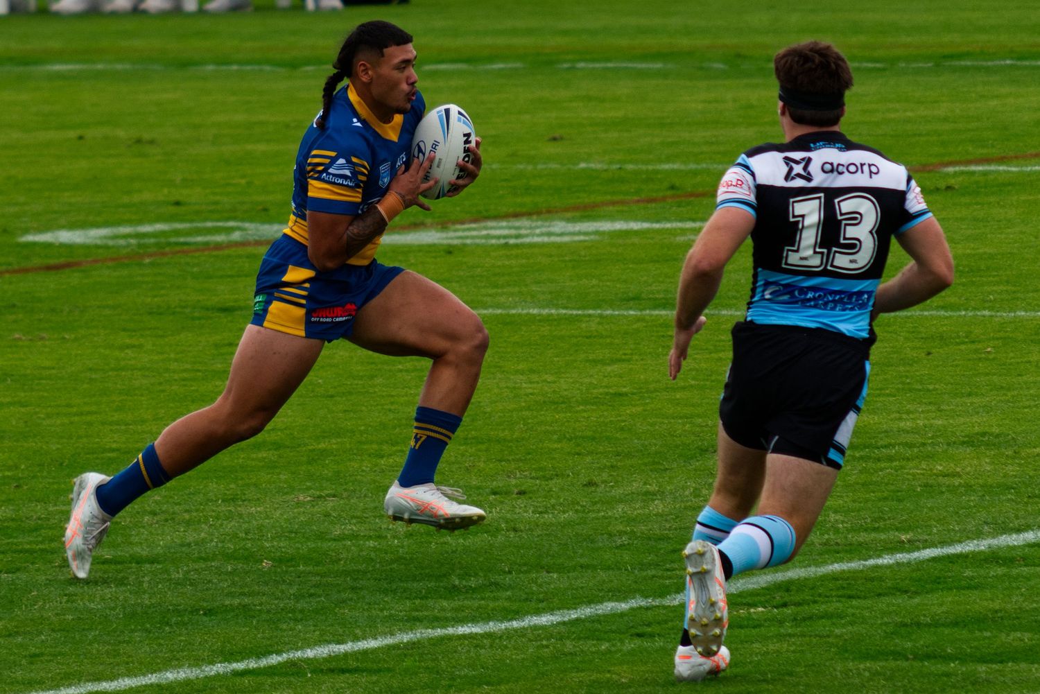 A rugby league player in blue and gold jersey runs with the ball during a match.