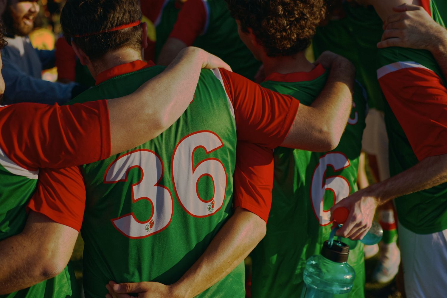 Soccer team huddles together in green and red jerseys, showing unity before a match.