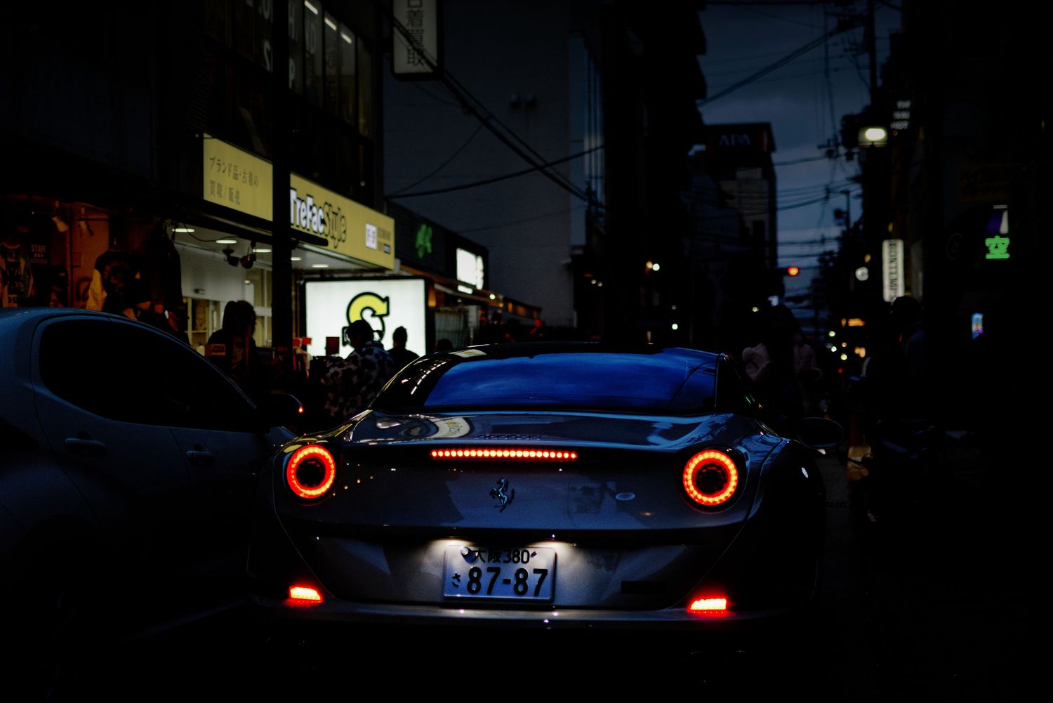Sports car with glowing red taillights parked on a dark city street at night.