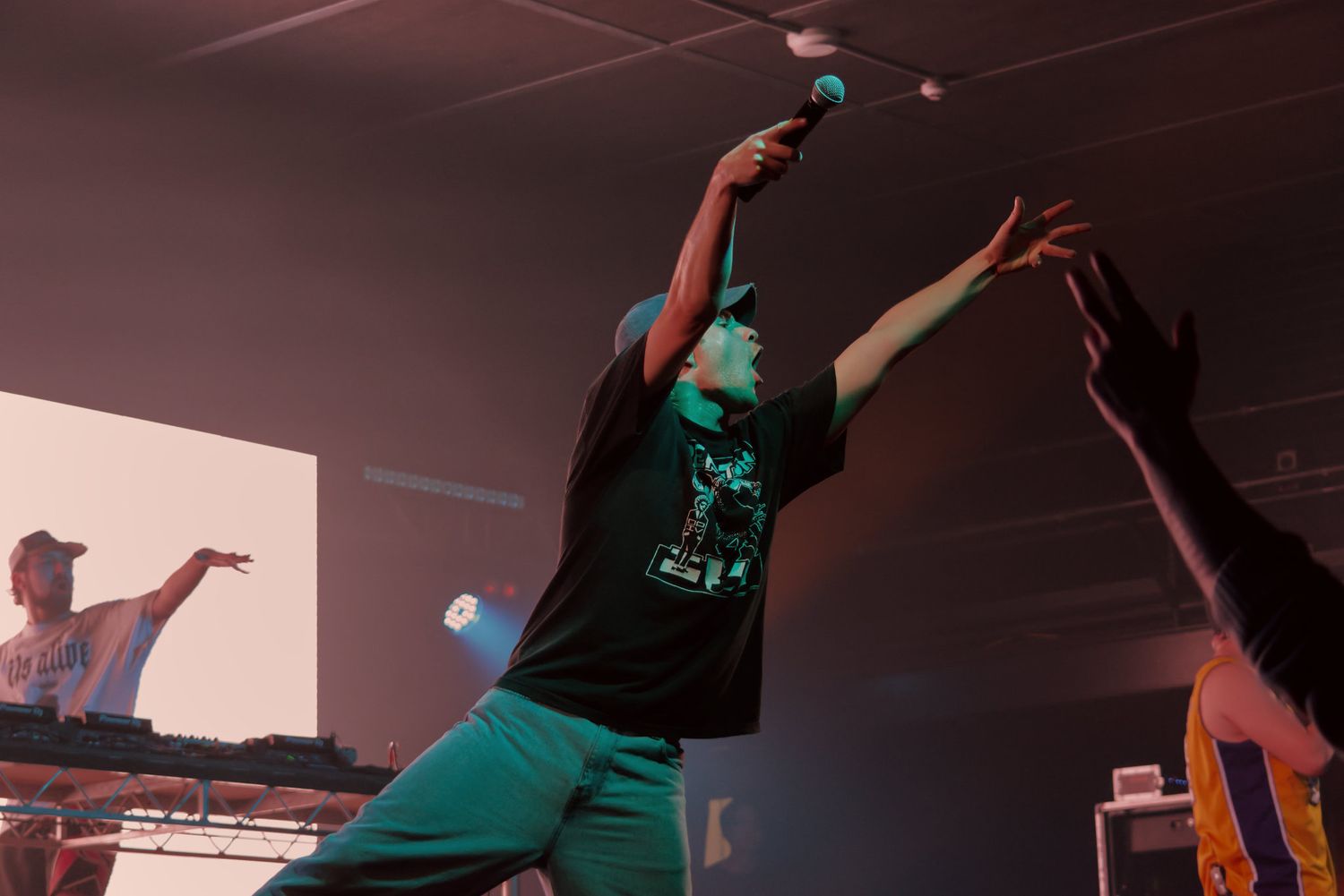 Hip-hop artist reaches toward crowd in teal pants during vibrant live stage performance.