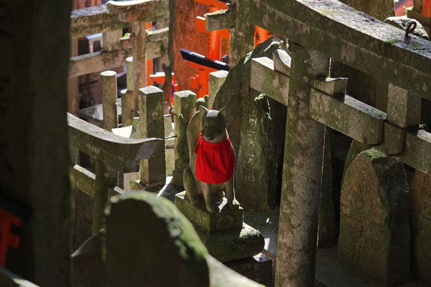 Woman in red dress walking through ancient stone torii gates at Fushimi Inari Shrine in Kyoto, Japan.