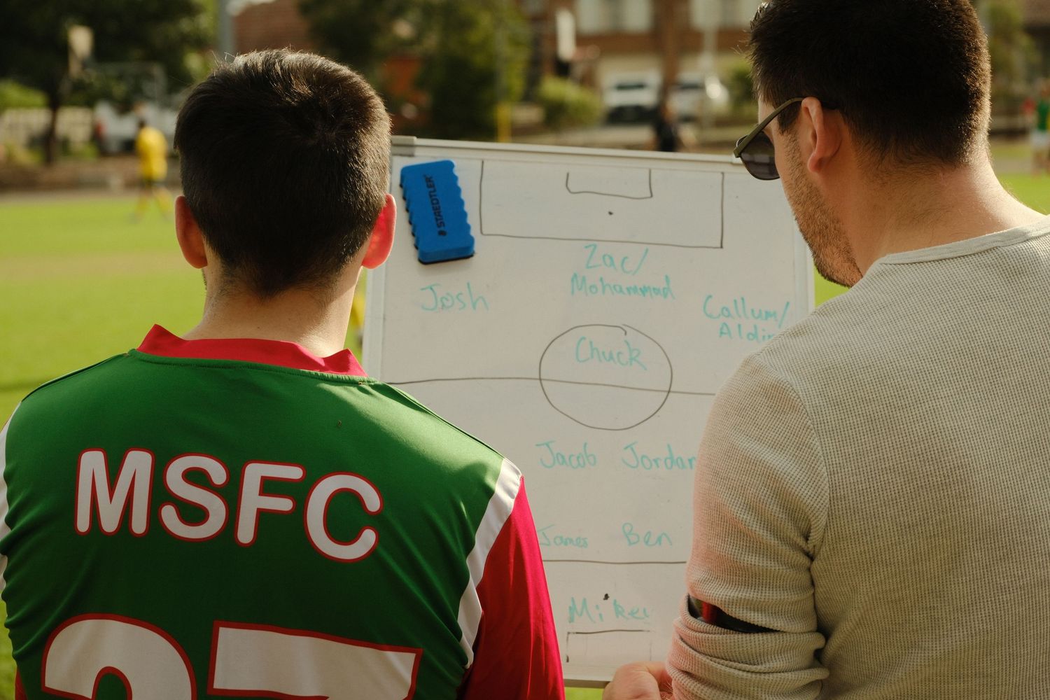 Soccer coach and player reviewing tactical formation on a whiteboard during an MSFC football training session outdoors.