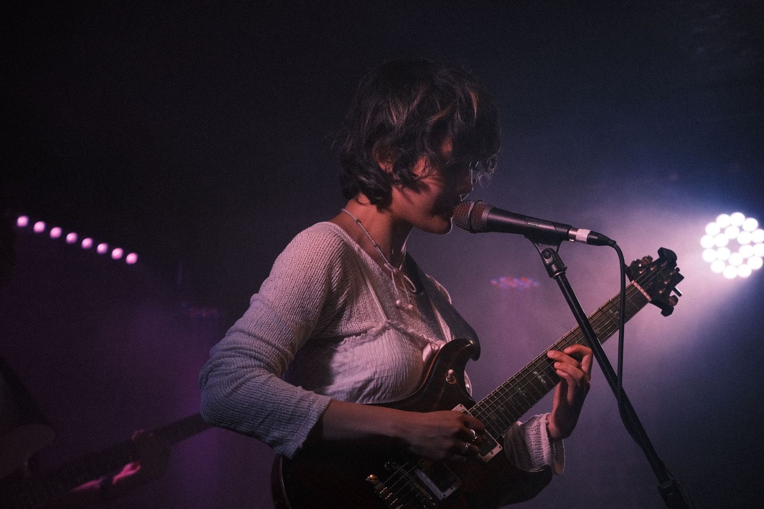 Female guitarist performing on stage with a black electric guitar at a live music concert under dramatic lighting.