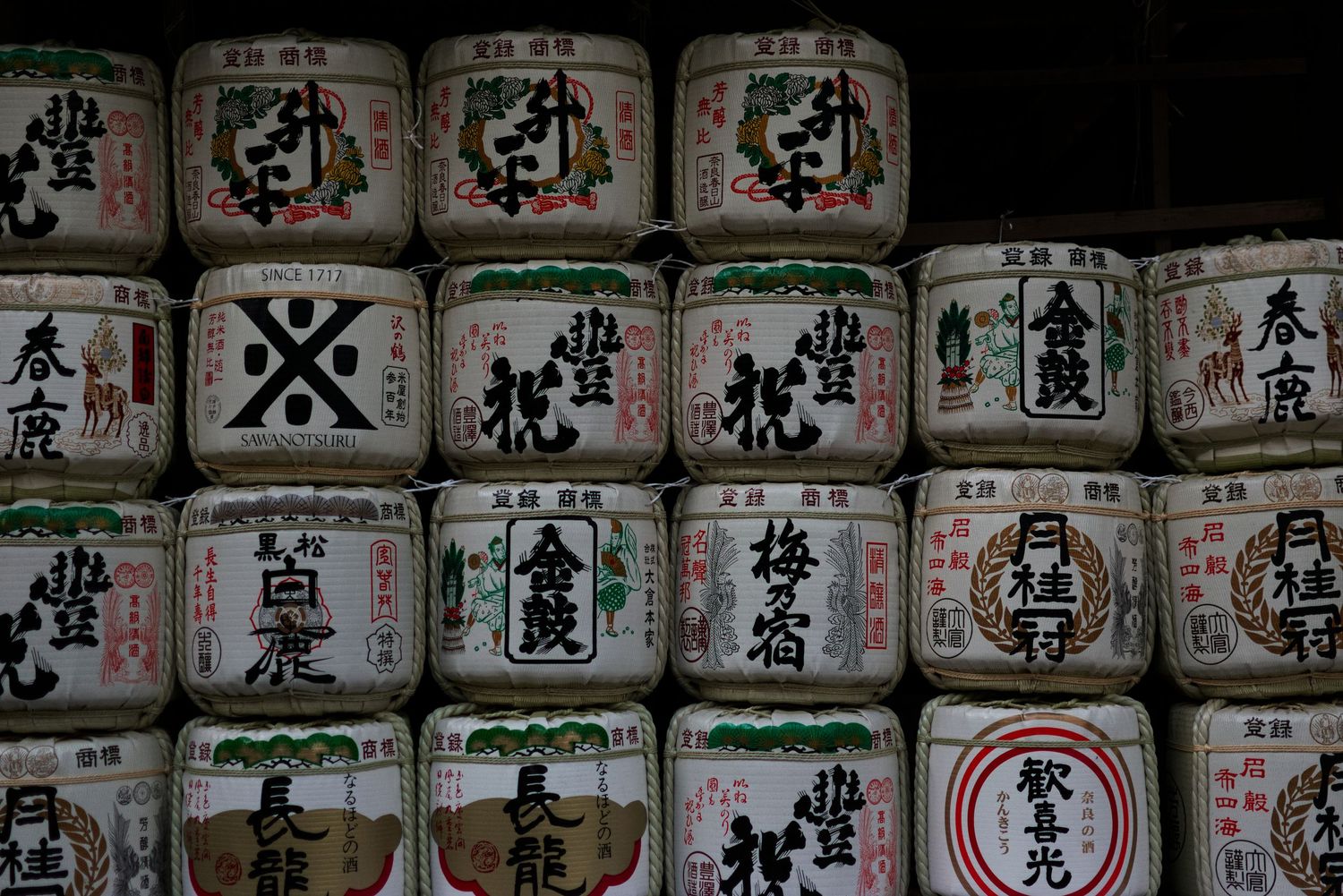 Rows of traditional Japanese sake barrels with colorful kanji labels stacked at a shrine.