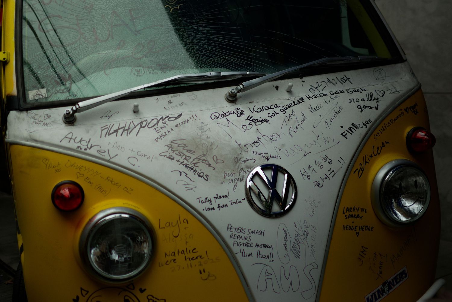 Yellow Volkswagen van hood covered in handwritten signatures and messages.
