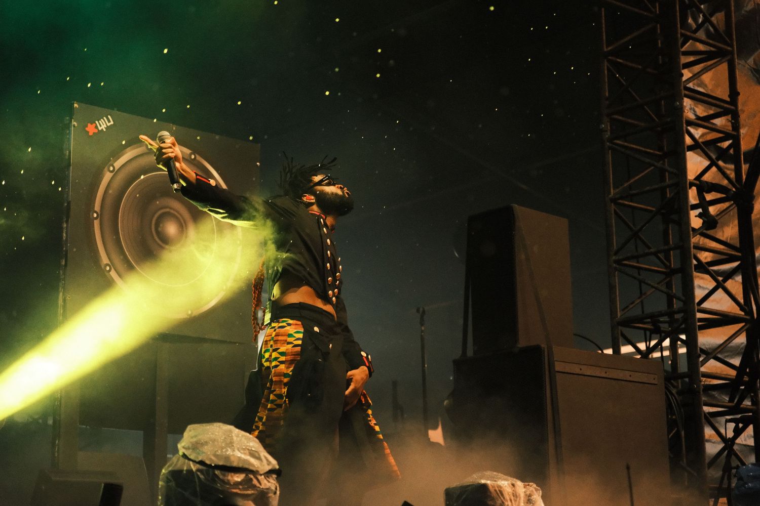 Performer in gold costume on stage with green laser lights at outdoor concert festival at night.