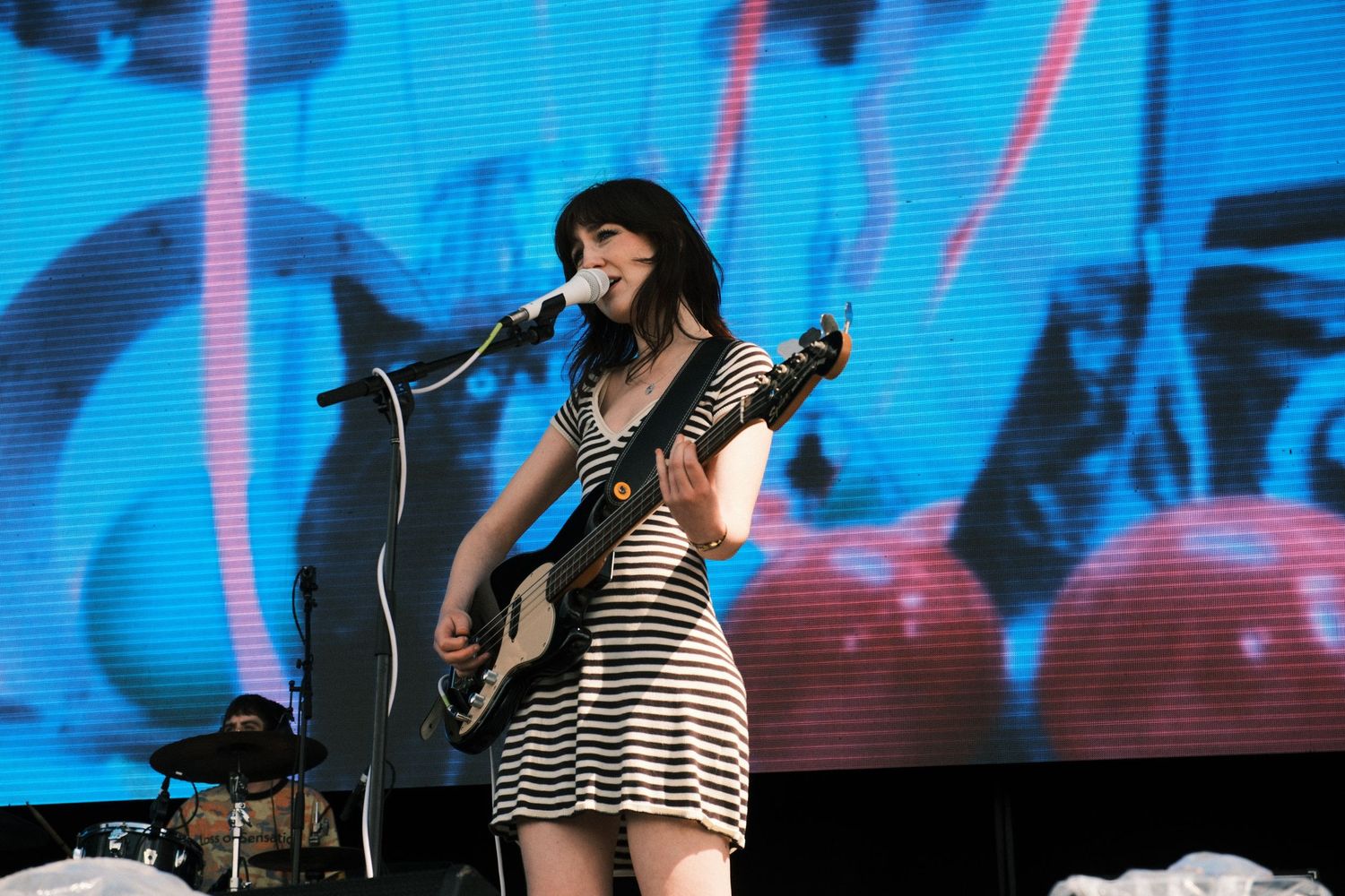 Woman in striped dress playing electric guitar and singing on stage at a live concert.