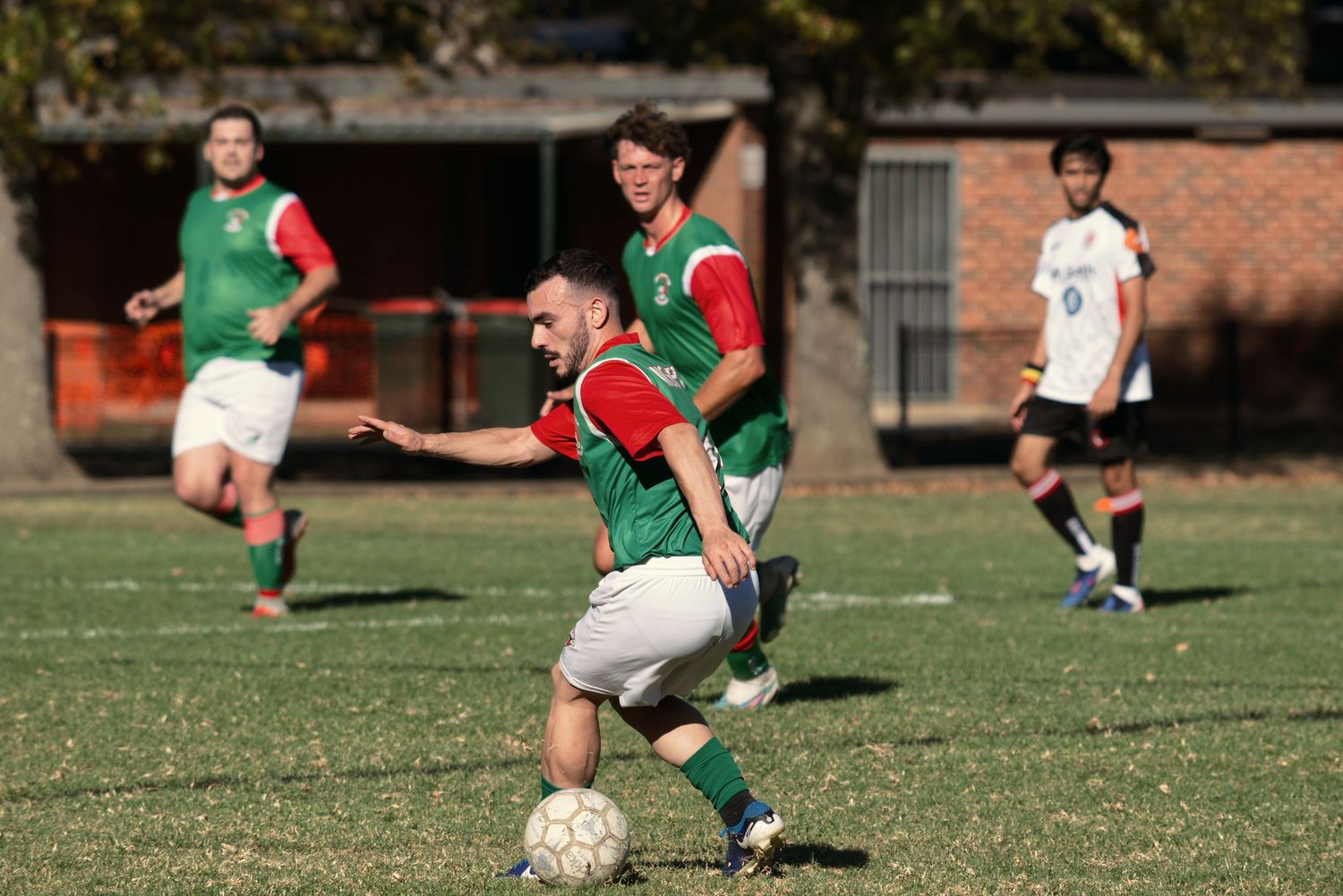 Soccer player in green and red jersey skillfully controls the ball during an outdoor game.