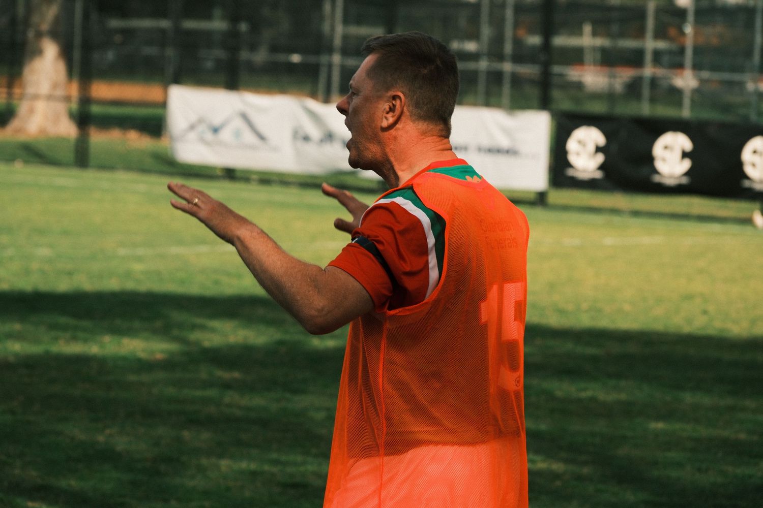 Soccer player in orange jersey gesturing on green field during outdoor match.
