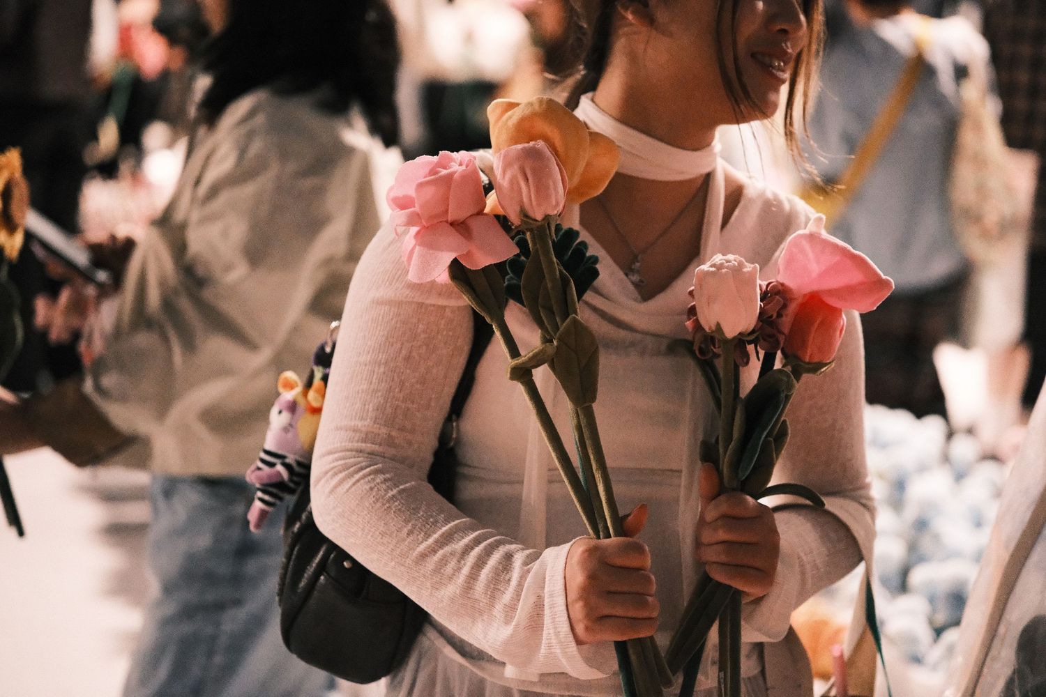 Young woman holding pink roses and tulips at a busy flower market.