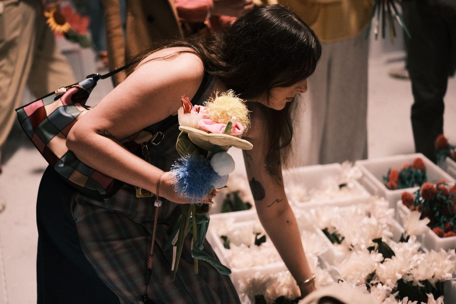 Young woman carefully selecting flowers from a display at an indoor flower market.