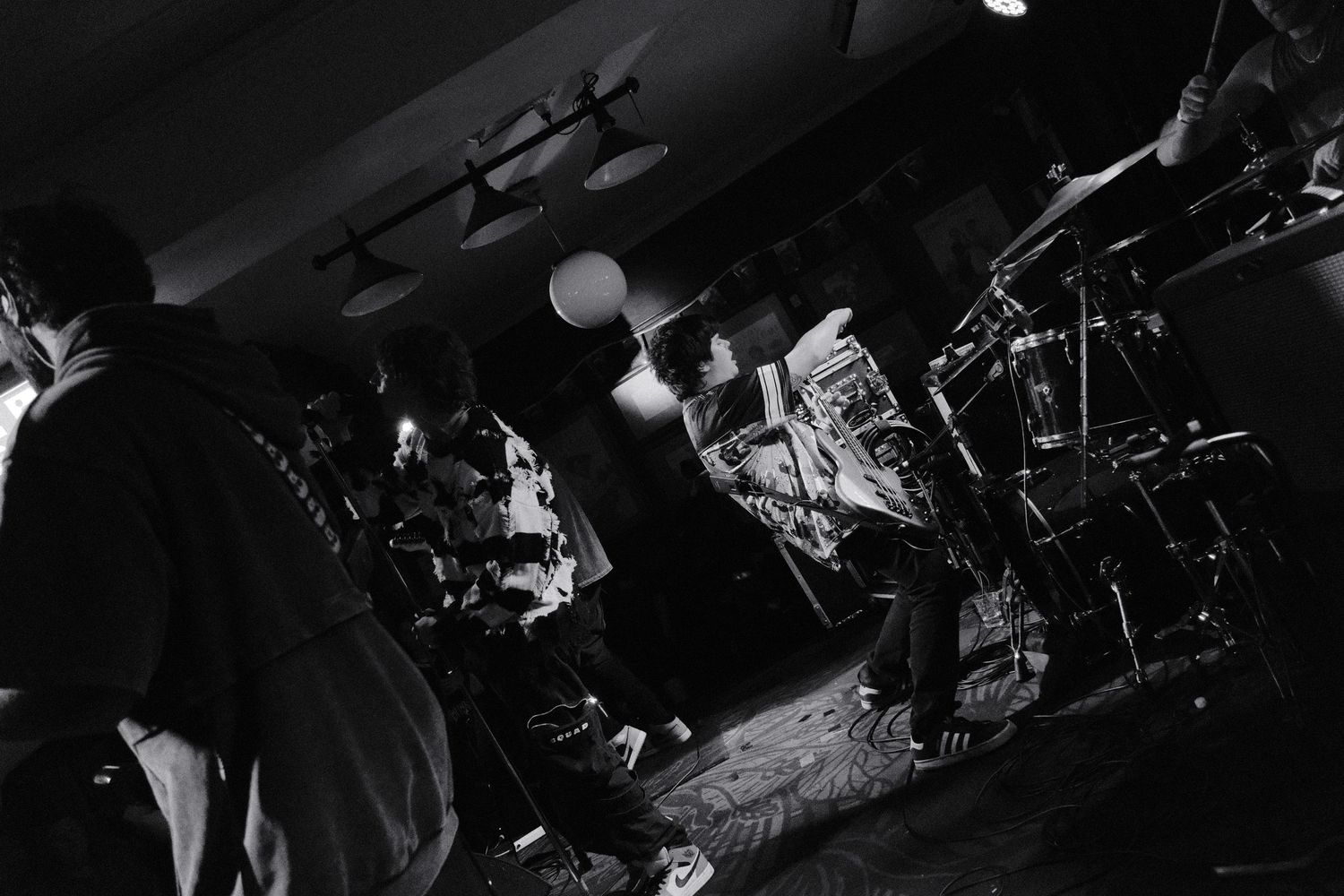 Black and white photo of a live band performing on a dimly lit stage with dramatic lighting.