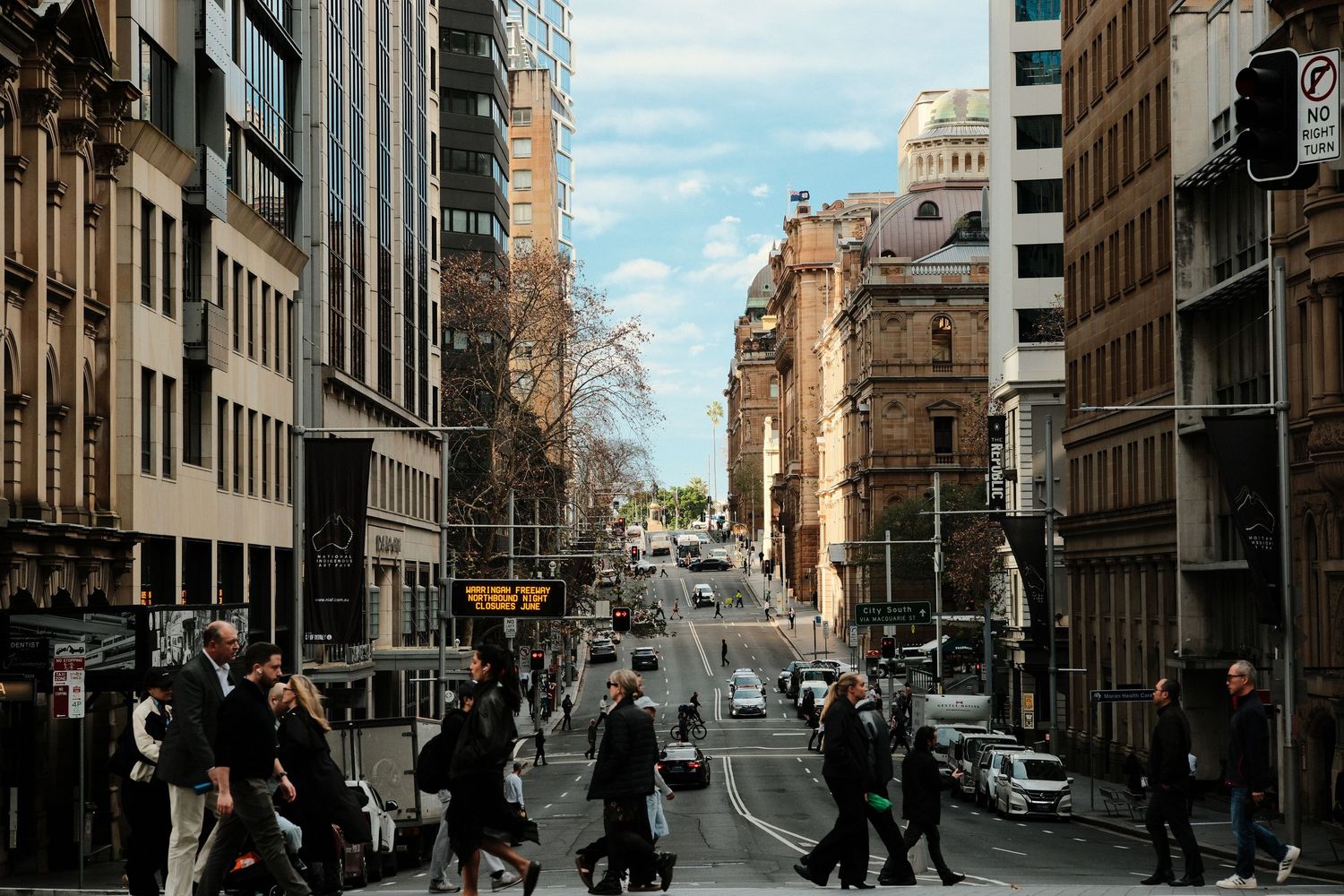 Busy city street crossing with pedestrians walking past tall buildings in a vibrant urban downtown district.