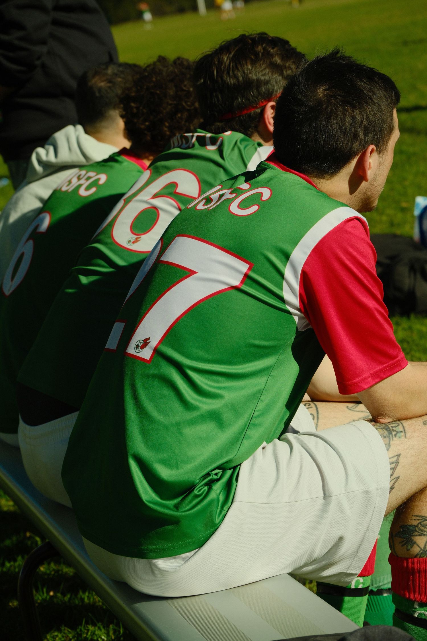 Soccer players in green and red jerseys numbered 6 and 7 sitting on a bench during a match.