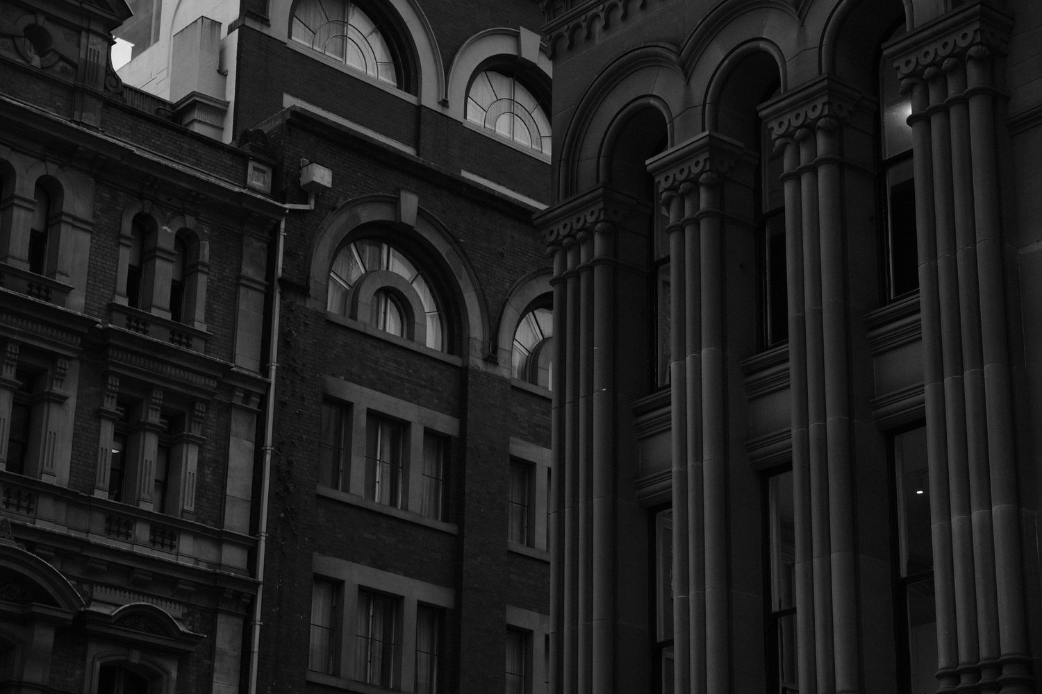 Black and white photo of ornate historic buildings with arched windows and tall columns in an urban setting.