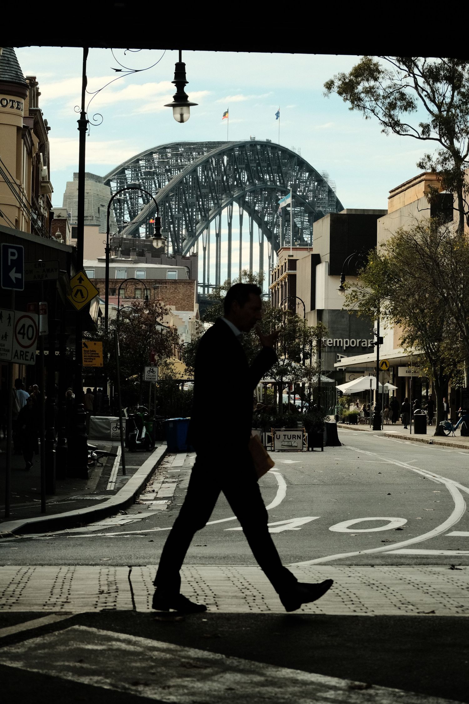 Silhouette of businessman crossing street with Sydney Harbour Bridge in background, The Rocks district, Australia.