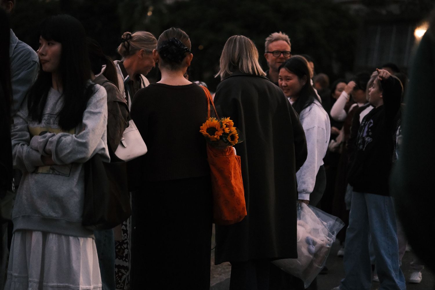Group of people gathered outdoors at dusk, one holding a bouquet of sunflowers.