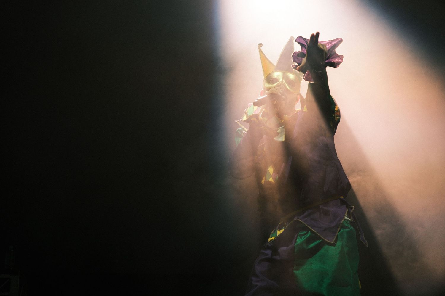 Performer in green costume with dramatic stage lighting and rays of light at a theatrical show.