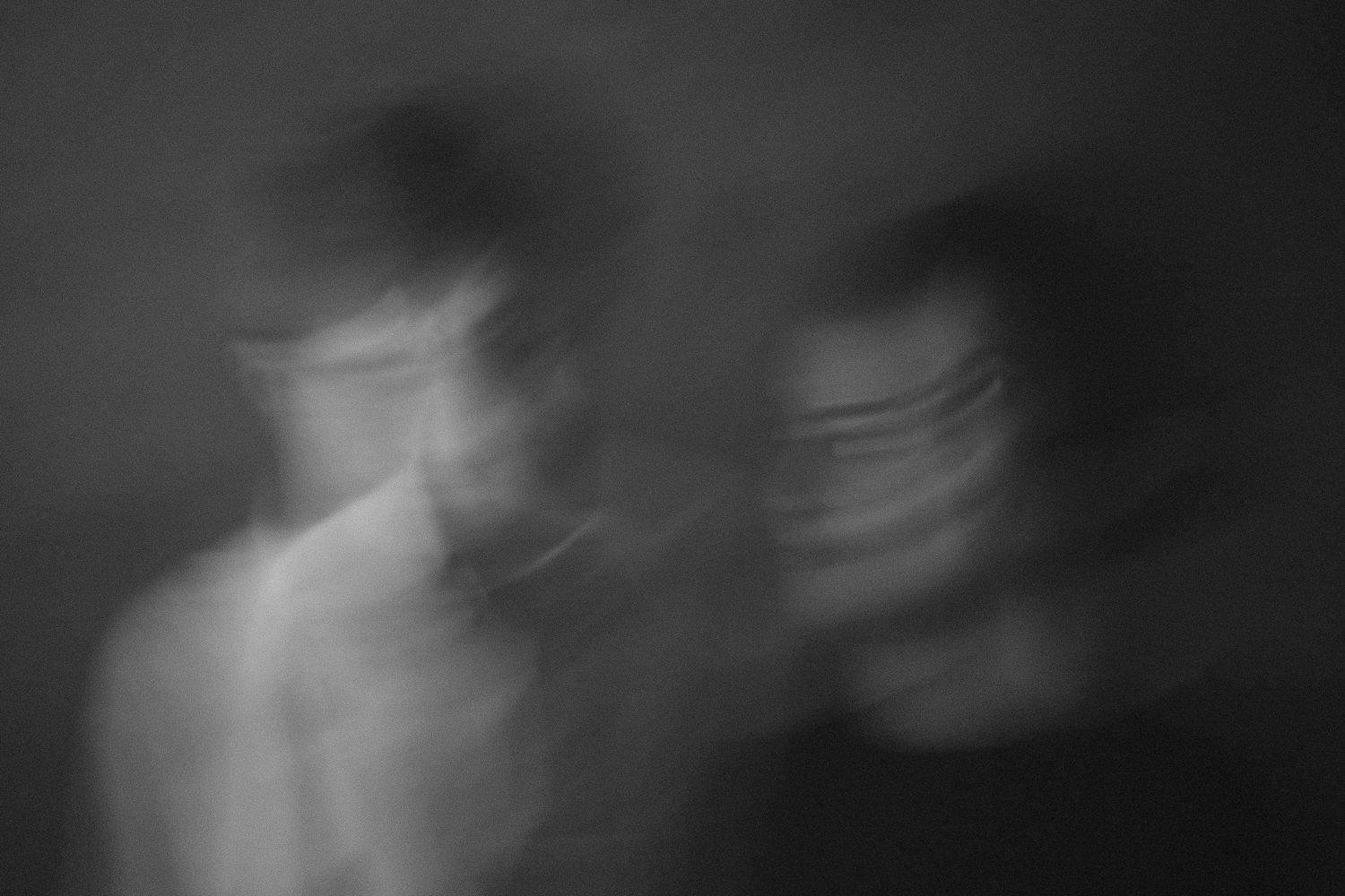 Blurry black and white double exposure portrait of two ghostly figures creating an eerie, surreal artistic effect.